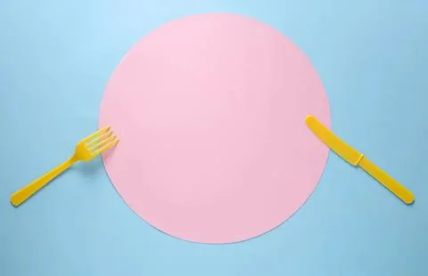 Empty pink round plate with yellow fork and knife on blue background Stock Photos