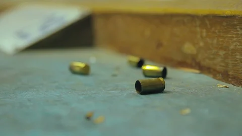 Empty pistol bullet shells dropping and impacting wooden table in a shooting  Stock Footage 128463873