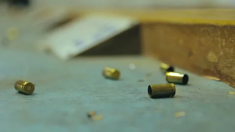 Empty pistol bullet shells dropping and impacting wooden table in a shooting  Stock Footage 128463887