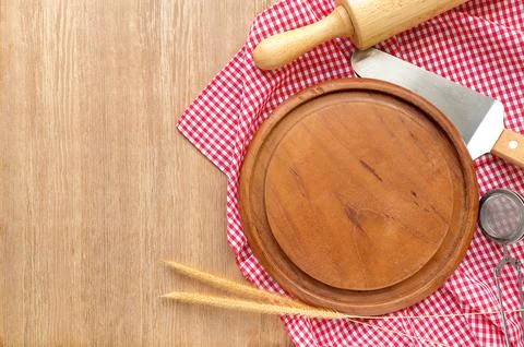 Empty pizza board, table cloth and wooden rolling pin on wooden table.  Stock Photos