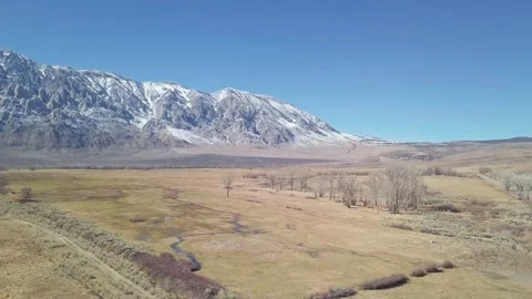 Empty plain farmland blue sky on Sierra Nevada snow covered rocky mountain Stock Footage 145088632