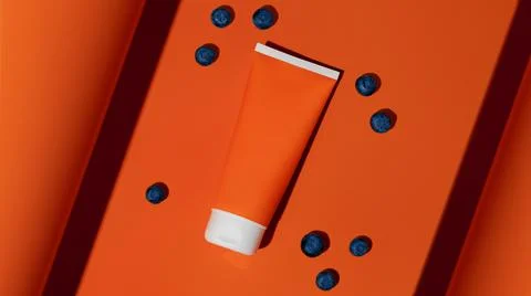 Empty plastic sun protection bottle with berries on orange background. Stock Photos