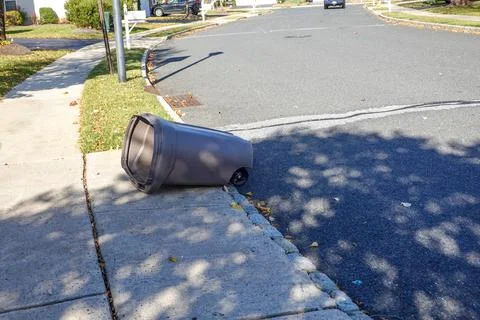 Empty plastic trash can laying on the ground on a driveway near a street in.. Stock Photos