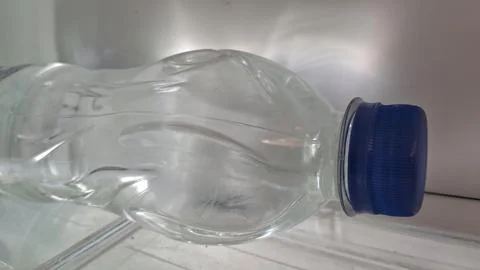Empty plastic water bottle lying on a cold refrigerator shelf surface Stock Photos