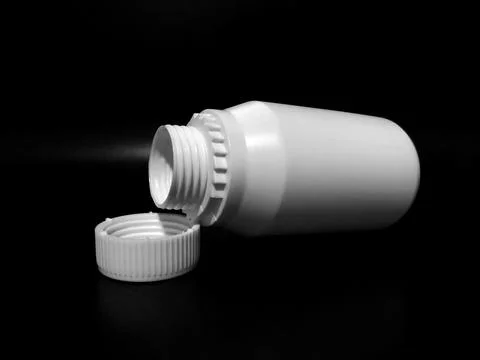 The empty plastic white bottle is on a dark background. Stock Photos