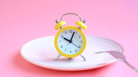 Empty plate with alarm clock and fork on pink background, intermittent fasting Stock Footage 229254694