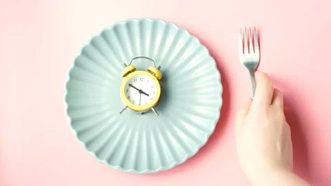 Empty plate with alarm clock and female hand on pink background, intermittent Stock Footage 236880815
