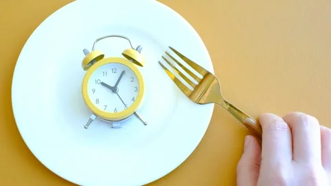 Empty plate with alarm clock and fork on brown background, intermittent fasting Stock Footage 302943440