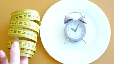 Empty plate with alarm clock and measuring tape on brown background close-up top Stock Footage 303027560