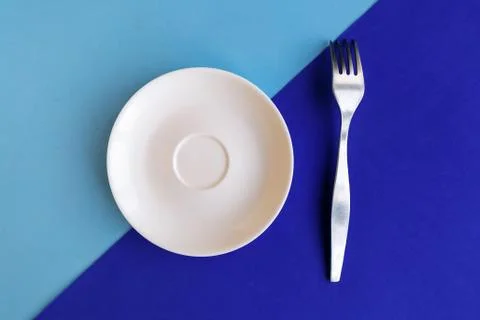 Empty plate and fork on blue background. Copy space for the text. Minimal con Stock Photos