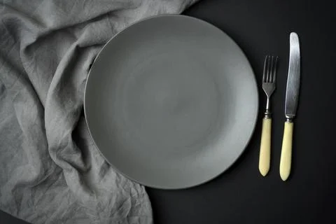 Empty plate on a dark background. Empty gray ceramic plate with a knife and fork Stock Photos