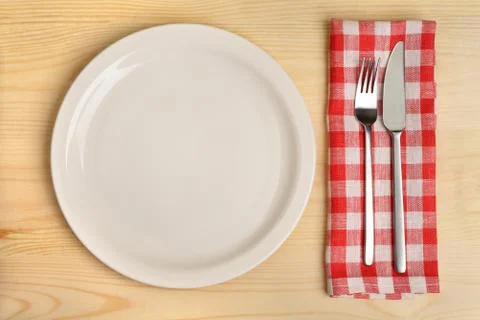 Empty plate with fork and knife on red checkered napkin on wooden background. Stock Photos