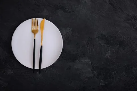 Empty plate with fork and knife on dark stone background. Gold and black tabl Stock Photos