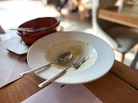 Empty plate with fork and spoon after meal in restaurant. Represents satisfac Stock Photos