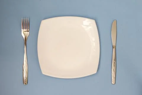 Empty plate, fork, knife on blue background. Clean plate and cutlery. Stock Photos