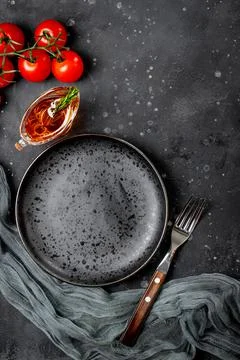 Empty plate, fork, tomatoes and oil in gravy boat on black background top view Stock Photos