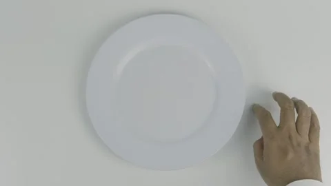 An empty plate with a hand tapping fingers on the table against a white back Stock Footage 303551816