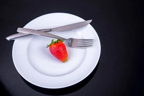 Empty plate with knife and fork an one lonely strawberry Foto stock