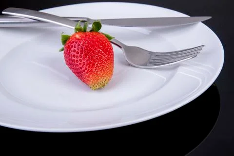 Empty plate with knife and fork an one lonely strawberry Stock Photos