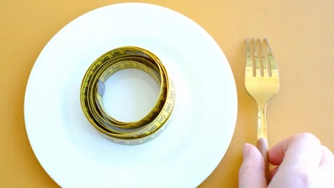 Empty plate with measuring tape and fork on brown background, intermittent Stock Footage 303537573