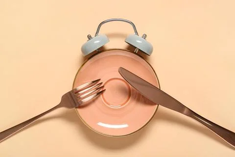 Empty plate in shape of alarm clock with cutlery on beige background. Intermi Stock Photos