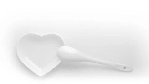Empty plate in the shape of a heart and a ceramic spoon on a white background Stock Photos