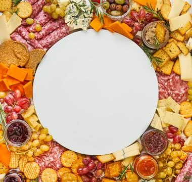 Empty plate surrounded by various cheeses, salami, crackers, top view Stock Photos