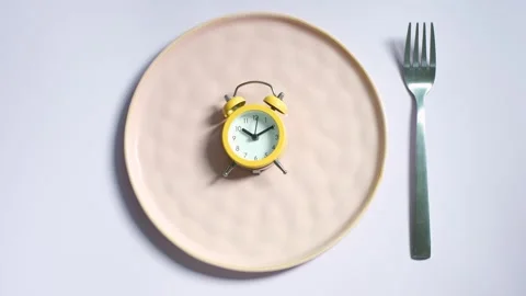 Empty plate with yellow alarm clock on lilac background top view close-up. Stock Footage 285579510