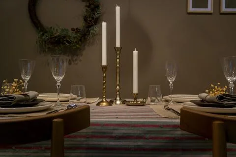 Empty plates and three candles stand on the table on a multicolored striped t Stock Photos