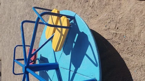 Empty playground carousel slowly spins under the sun. The scene reflects urban 動画素材 307920727
