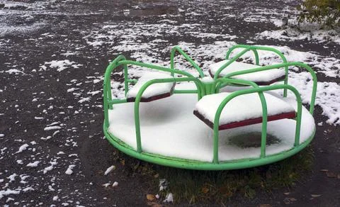 An empty playground, a small carousel covered with fallen first snow Stock Photos