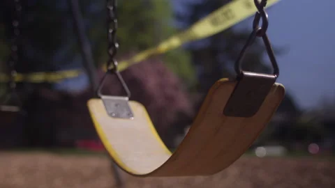 An empty playground swing blowing in the wind with caution tape Video stock 130382118
