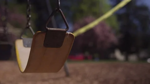 Empty playground swing with caution tape blowing in the wind in the background Video stock 130381762