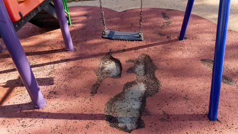 Empty playground swing over worn rubber safety flooring with damaged surface Stock Photos