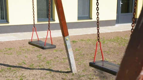 Empty playground swing set gently moving in a lonely schoolyard during spring Stock Footage 338443980