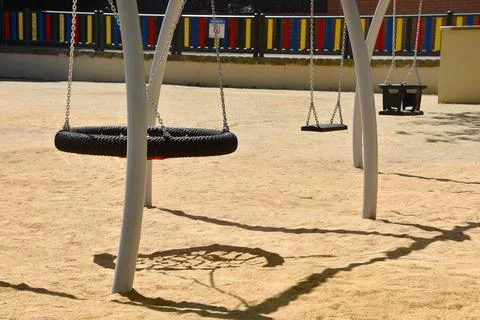 Empty playground swings casting shadows on sandy ground, summer playground an Stock Photos
