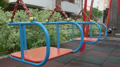 Empty playground, two red-blue swings, second swing is motionless. Stock Footage 229893683