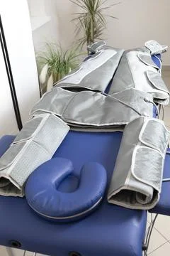 Empty pressure therapy gray massaging suit on blue couch in spa, treatment of Stock Photos