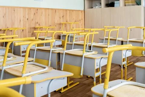 An empty primary school classroom features yellow desks stacked with chairs.. Stock Photos