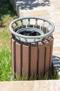 Empty public trash can in park with grass and pavement Stock Photos