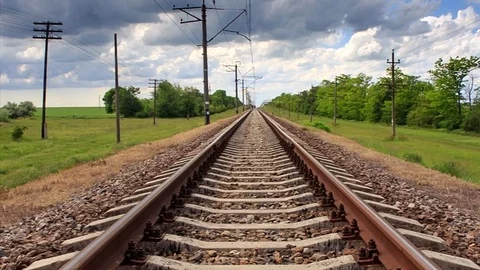 Empty railway tracks go through green field with posts under cloudy sky. Stock Footage 75959242