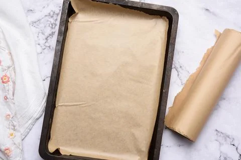 Empty rectangular metal baking sheet and roll of brown parchment paper on whi Foto stock