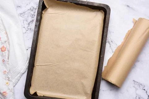 Empty rectangular metal baking sheet and roll of brown parchment paper on ... Stock-Fotos
