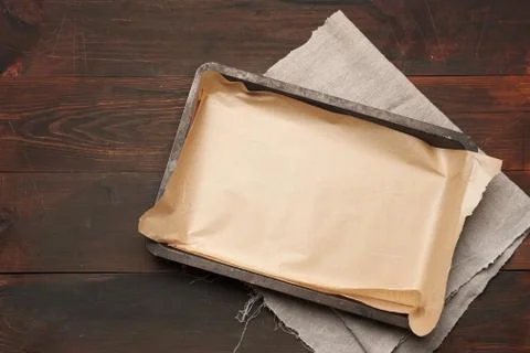 Empty rectangular metal pan covered with brown parchment paper on a wooden ta Foto stock
