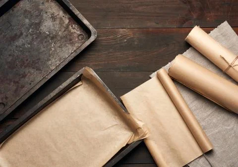 Empty rectangular metal pan covered with brown parchment paper and paper roll Stockfoto's