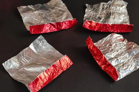Empty red and silver candy wrappers on a black background. Crumpled foil from Stock Photos