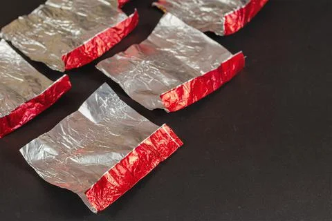 Empty red and silver candy wrappers on a black background. Crumpled foil from Stock Photos