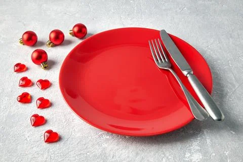 Empty red ceramic plate with cutlery surrounded by red Christmas balls and .. Foto stock