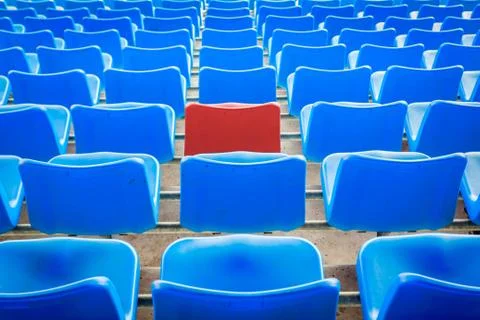 An empty red chair, arounded by blue chairs at the football Stadium Stock Photos