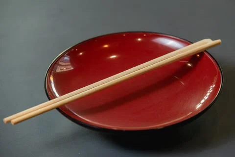 Empty red dish with chopsticks on grey background. Stock Photos